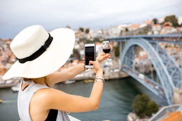 Young woman tourist photographing a glass of Porto wine sitting on the terrace with great cityscape...