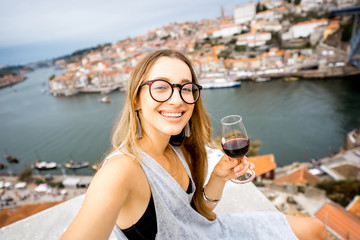 Fototapeta na wymiar Portrait of a young and happy woman enjoying Porto wine, sitting on the terrace with beautiful cityscape view in Porto, Portugal
