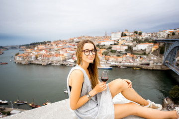 Fototapeta na wymiar Portrait of a young and happy woman enjoying Porto wine, sitting on the terrace with beautiful cityscape view in Porto, Portugal