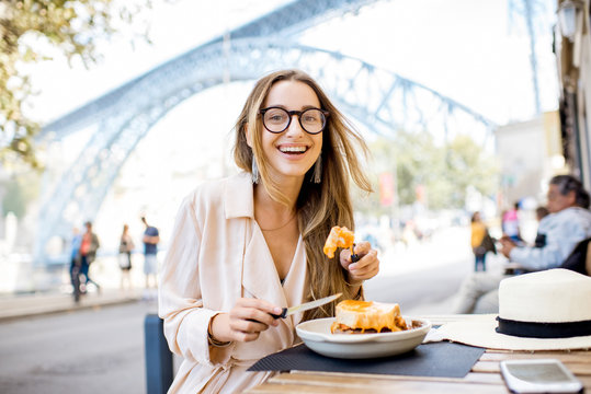 Woman eating traditional portuguese sandwich with meat called francesinha sitting at the restaurant in Porto city, Portugal