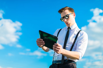 Naklejka na ściany i meble Attractive busunessman in white shirt, tie, braces and sunglasses look in tablet