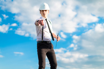 Young attractive foreman in white helmet, tie and braces stand on the roof with tablet