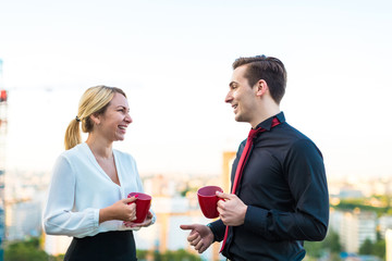 Couple of businessmen, attractive brunette man and pretty blonde woman stand on the roof and drink coffe