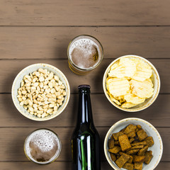 Dark beer in a bottle and light in glasses on a wooden table next to salty snacks - chips, peanuts and crackers