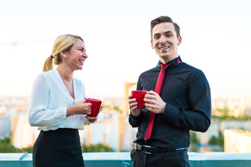 Couple of businessmen, attractive brunette man and pretty blonde woman stand on the roof and drink coffe