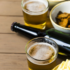 Dark beer in a bottle and light in glasses on a wooden table next to salty snacks - chips, peanuts and crackers