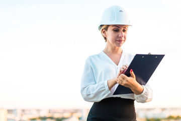 Pretty young forewoman in helmet stand on the roof with tablet in hands