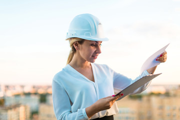 Pretty young forewoman in helmet stand on the roof with tablet in hands