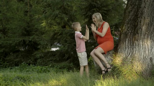 Pregnant mother plays with her son by the tree. They embrace and rejoice in life.