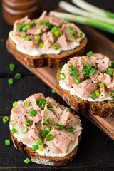 Open sandwiches with cottage cheese, canned tuna and green onions on black wooden background.