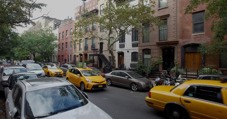 Fototapeta na wymiar Wide view exterior shot of a typical generic New York City block with apartment buildings yellow taxi cab traffic and parked cars lining side of street.