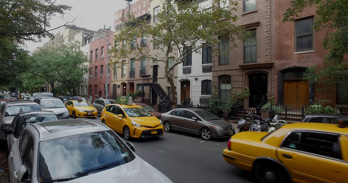 Wide view exterior shot of a typical generic New York City block with apartment buildings yellow taxi cab traffic and parked cars lining side of street. © Brandon Klein