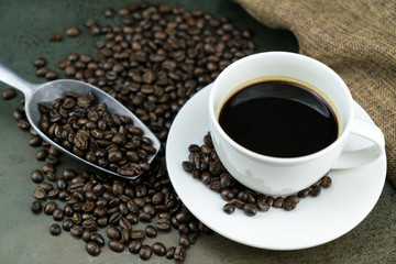 Hot coffee in the white cup with roast coffee beans, bag and scoop on stone table background