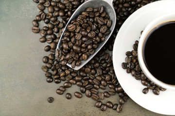 Hot coffee in the white cup with roast coffee beans and scoop on stone table background