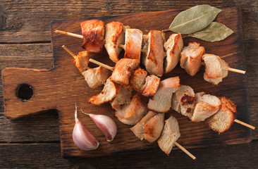 Slices of baked meat with garlic and laurel on wooden cutting board on old wood surface.
