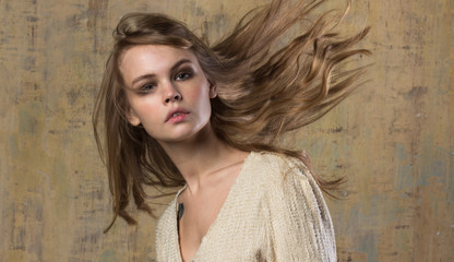 Fototapeta premium A beautiful young model with flying hair in a stylish beige dress. An image in beige tones.