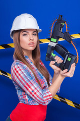 Young sexy builder girl in chechered shirt, white helmet and jeans stand with nail gun