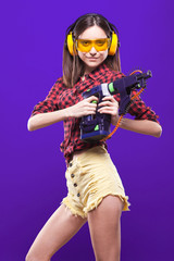 Young pretty sexy girl in red chechered shirt, build goggles and earmuffs hold perforator