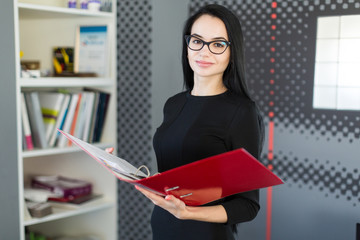 Beautiful young businesswoman in black dress and glasses hold paper folder