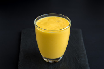Fresh mango smoothie on a black slate background.