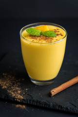 Fresh mango smoothie with cinnamon on a black slate background.