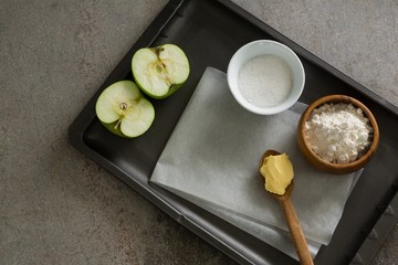 Bowl of sugar and apple, flour with butter in spoon