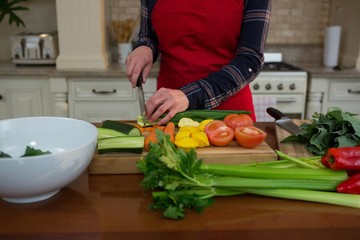 Mid section of woman cutting vegetable in kitchen