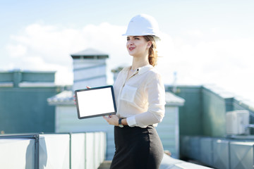 Attractive businesslady in white blouse, watch, helmet and black skirt stand on the roof and show empty tablet