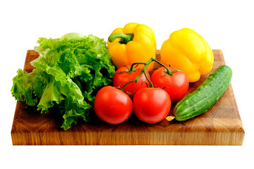 Branch of fresh red tomatoes, yellow bell pepper, green cucumbers and lettuce on a wooden cutting board isolated on white
