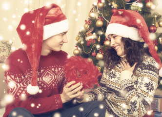 Happy couple sit near christmas tree and decoration at home. Winter holiday and love concept. Yellow toned with snow.