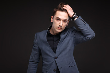 Obraz premium Handsome serious businessman in grey jacket, costly watch and black shirt, black background