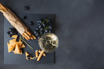 Cheese plate served with crackers, grapes and glass of white wine on dark background.