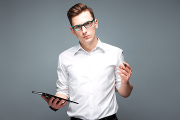 Handsome young businessman in costly watch, black glasses and white shirt hold tablet and pen