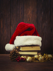 Obraz na płótnie Canvas Santa Claus hat, books, fir cone, juicy viburnum, decorative boxes, balls and beads. Focus on the Santa Claus hat. Added effect