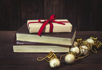 A packing box with a gift bandaged with red ribbon, books, golden balls, decorative boxes and beads. Focus on the gift