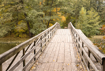 Fototapeta na wymiar Wooden bridge though the lake. Fall forest behind the lake.