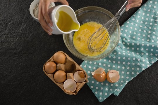 Woman Adding Oil Into Beaten Eggs In A Bowl