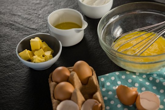 Beaten eggs, egg tray, butter, oil and flour kept on a black