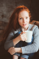 happy young readhead woman drinking hot coffee or tea at home. Calm and cozy weekend in winter or autumn