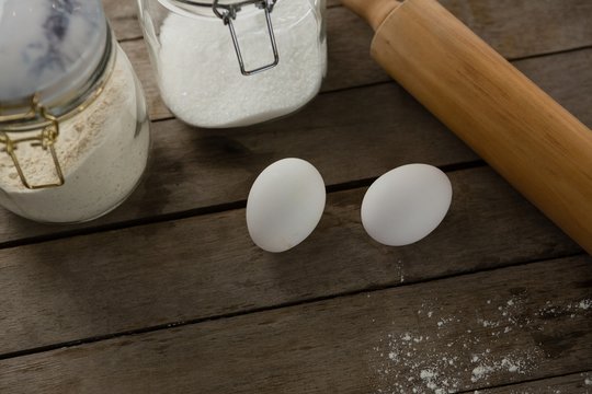 Rolling pin, eggs and glass containers on a wooden table