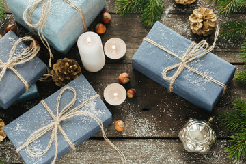 Festive Gifts with Boxes, Candle, Snow, Coniferous, Basket, Cinnamon, Pine Cones, Nuts on Wooden Background.