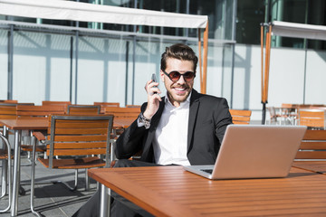 Male businessman or worker in black suit at the table and talking on phone