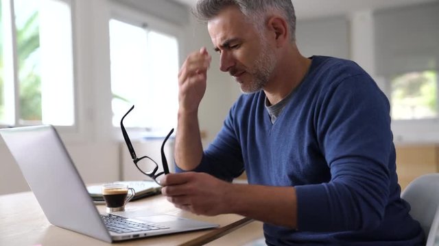 Man at home having a headache in front of laptop