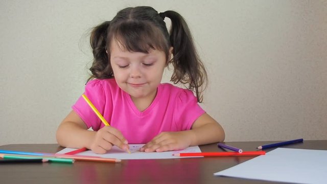 A happy child paints with colored pencils. Beautiful little girl with colored crayons.