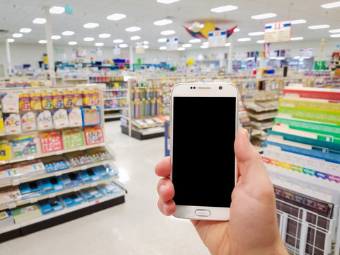 Hand holding mobile smart phone on Office supply shelf in store blur background