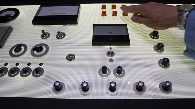 HAND ADJUSTS AN AMBIGUOUS CONTROLE PANEL.  Slow dolly shot.