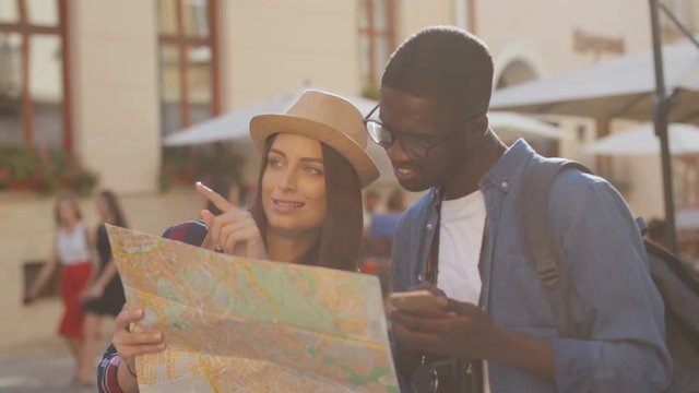 Lost young cute couple looking at the city map standing in centre of town. Young man using smartphone for navigation. Multi-ethnic.