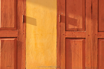 Fototapeta premium Orange retro thai wooden folding door with yellow wall under evening sunlight