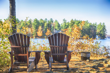 Naklejka premium Two Muskoka chairs on a wood dock at a blue lake