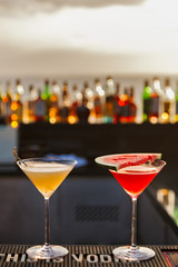 A pair of watermelon cocktail and sidecar orange cocktail at evening sunlight with ocean and bar background